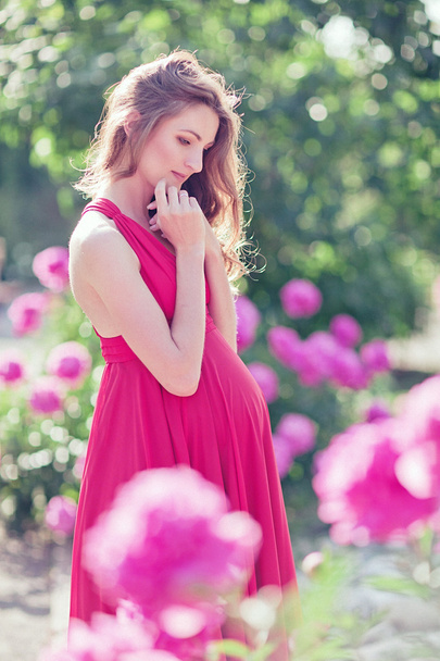 Pregnant woman in blooming garden of peony - Fotó, kép