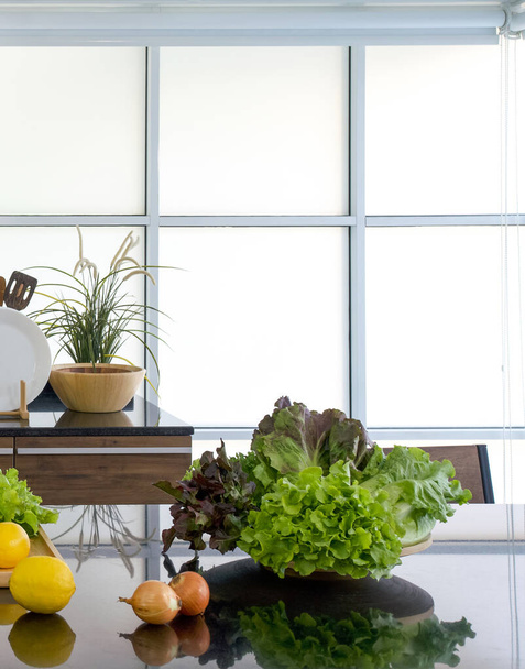Un tazón de verduras frescas lugar en la encimera de cocina de granito brillante negro. Ambiente matutino en una cocina moderna - Foto, Imagen