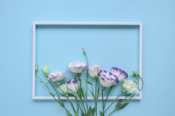 Beautiful eustoma flowers on blue pastel background with white frame. Minimal style composition. Nature backdrop for seasonal cards, blogs, web design. Top view. Flat lay - Foto, imagen