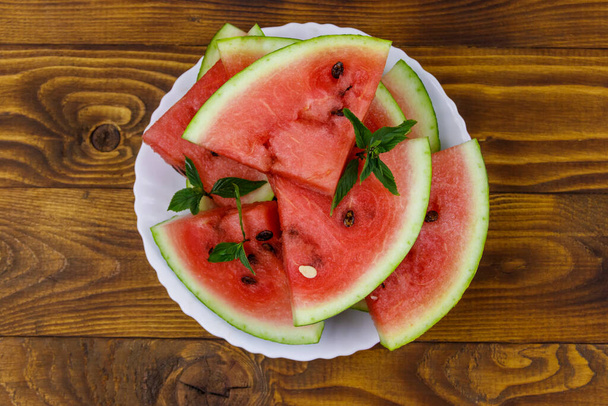 Frisch gereifte, in Scheiben geschnittene Wassermelone in weißem Teller auf einem Holztisch. Ansicht von oben - Foto, Bild