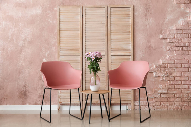 Moderni nojatuolit ja kukkakimppu pöydällä lähellä väriä seinään - Valokuva, kuva