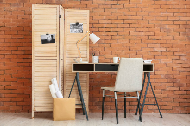 Σύγχρονη χώρο εργασίας και πτυσσόμενα οθόνη κοντά τοίχο από τούβλα - Φωτογραφία, εικόνα