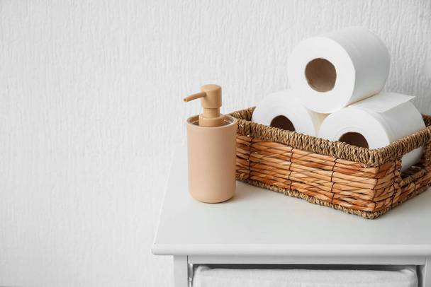 Cesta com rolos de papel higiênico e garrafa de produto cosmético na mesa no banheiro - Foto, Imagem