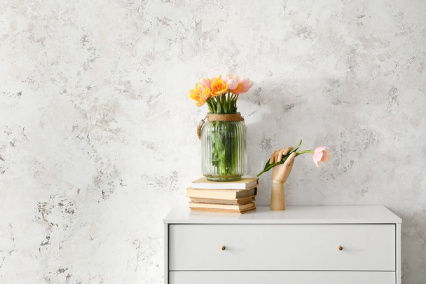 Holzhand mit schönen Tulpenblumen auf der Kommode in der Nähe der Lichtwand - Foto, Bild