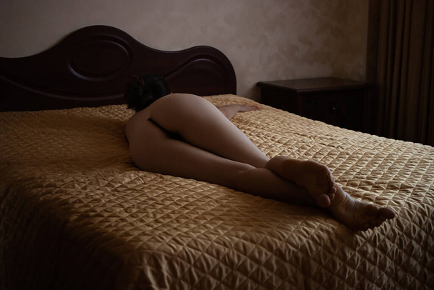 Back view of slim sexual nude woman in panties lying on bed in room - Foto, Imagen
