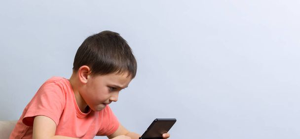 close up of young boy playing handheld video game at a table with some decoration. Against grey background - Photo, Image