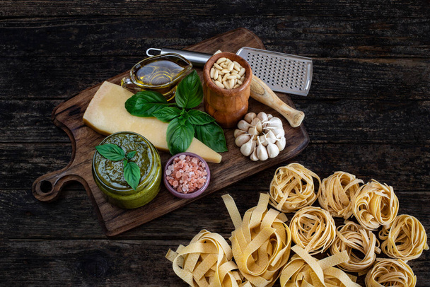 Pesto saus bereiding op de houten tafel. Basilicum, pijnboompitten, mortel, parmezaanse kaas en een rasp op het aanrecht. - Foto, afbeelding