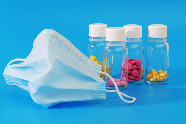 protective face mask and various pills in glass bottles on blue background - Φωτογραφία, εικόνα
