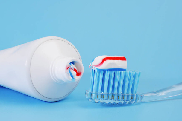 toothbrush with tricolor toothpaste on it and white toothpaste tube on blue background - Φωτογραφία, εικόνα