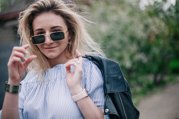 Young blonde in leather jacket and sunglasses posing in the street - Fotoğraf, Görsel