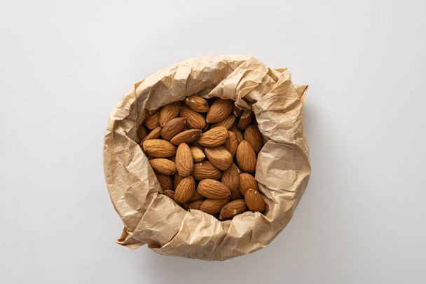 almonds in craft paper, keto food, on white background, top view, empty space for text - Photo, Image