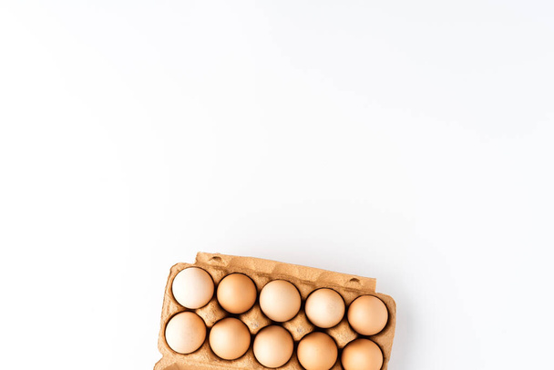 Overhead shot of chicken eggs in carton box on white table  - Фото, зображення