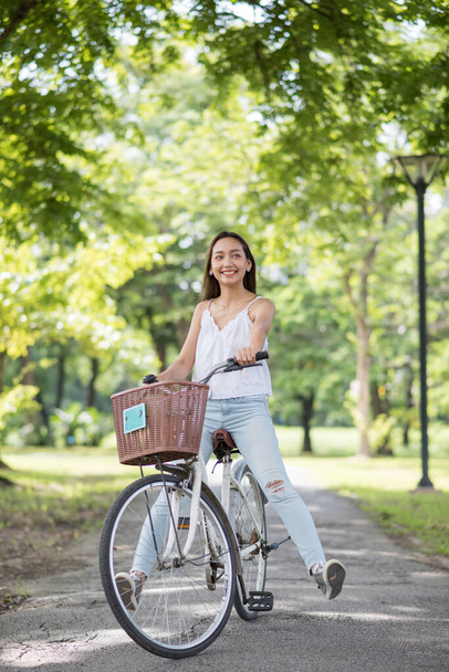Asian Beautiful funny  woman legs up riding bicycle at park with sunlight and foliage bokeh background in summer. People exercise and sport lifestyle concept. Portrait of happy girl in garden. - Fotó, kép
