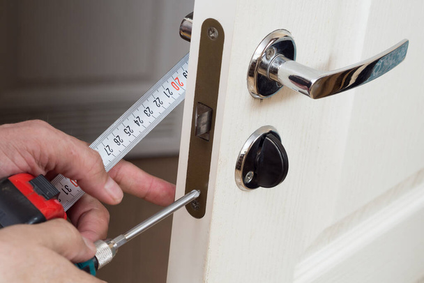 Worker installing or repairing new lock and door knob with screwdriver. Locksmith repair or install the door lock in house. - Foto, imagen