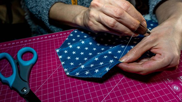 hands with needle and thread stitching a blue fabric with little stars - Photo, Image