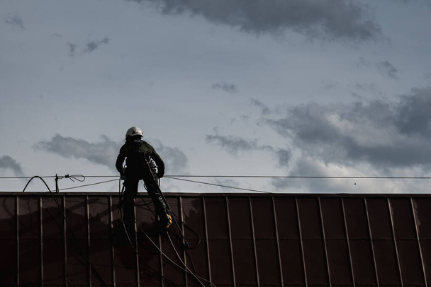 Ein Mann wäscht in luftiger Höhe ein Dach mit Druckwasser. Schutz eines Arbeitnehmers, der in einer Höhe arbeitet - Foto, Bild