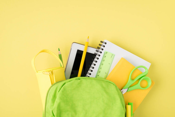 Photo aérienne du sac à dos règle bloc-notes stylo crayon comprimé et boîte à crayons isolé sur le fond jaune - Photo, image