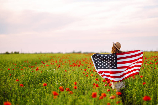 A fiatal nő büszkén lengeti az amerikai zászlót a mákmezőn. A hazafi felemeli a nemzeti amerikai zászlót a kék ég ellen. Függetlenség napja, július 4.. - Fotó, kép