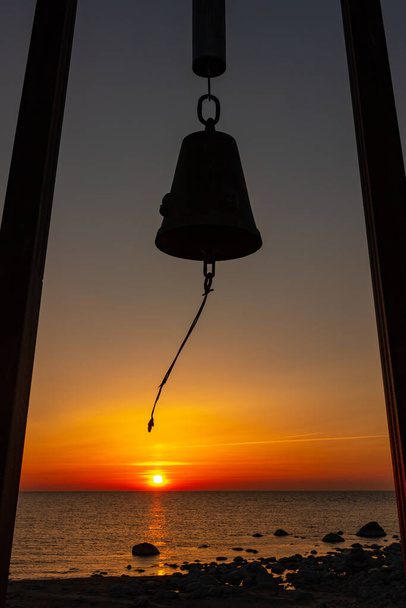 Pionowe zdjęcie dzwonowej sylwetki pomnika dla dzieci zagubionych w katastrofie promu Estonia na półwyspie Tahkuna, wyspa Hiiumaa, archipelag Moonsund, Estonia. Sylwetka dzwonów poruszająca się w wietrze podczas zachodu słońca w morzu - Zdjęcie, obraz