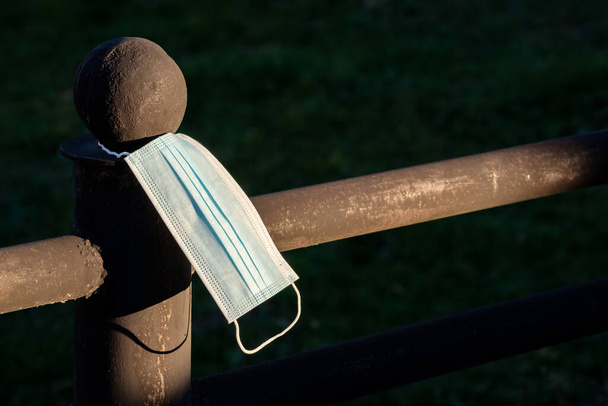 Tıbbi bir maskenin takıldığı karanlıktan çıkan bir çit. salgın atık sorunu - Fotoğraf, Görsel