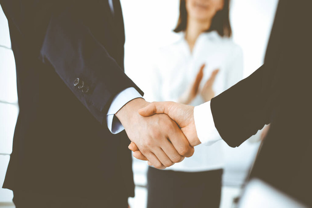 Businessman and woman shaking hands with colleagues at the background. Handshake at meeting in office. Concept of success in business - Foto, Imagem