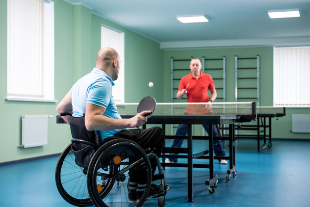 Adult disabled man in a wheelchair play at table tennis with his coach - Photo, Image