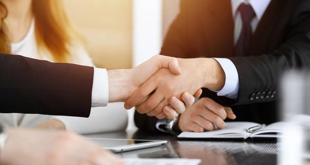 Businessman shaking hands with his colleague above the glass desk in sunny modern office, close-up. Unknown business people at meeting - Photo, image