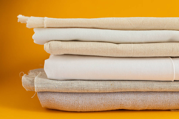 natural fabrics of ivory color - linen and cotton are stacked in a pile lie on a yellow background close-up - Photo, Image