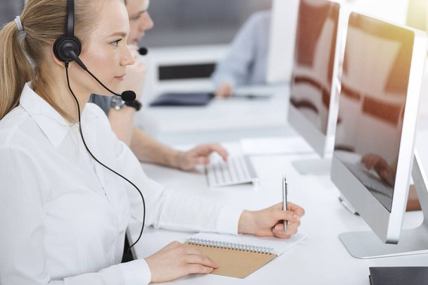 Call center. Group of casual dressed operators at work. Blond business woman in headset at customer service office. Telesales in business - Фото, зображення