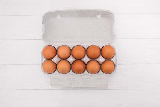 chicken eggs in a cardboard tray on a white wooden background. View from above. - Photo, Image