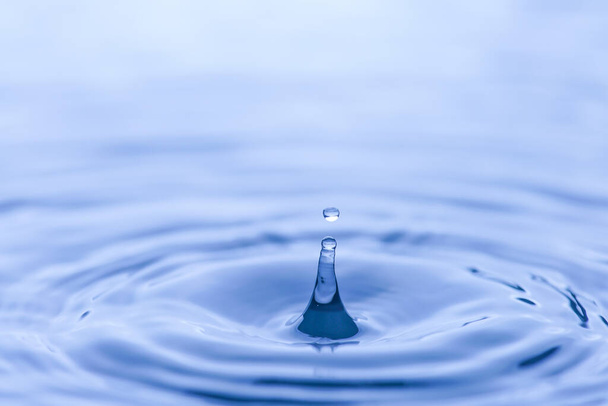 goccia d'acqua spruzzare in un bicchiere blu colpo colorato di acqua che gocciola e riflette l'acqua. - Foto, immagini