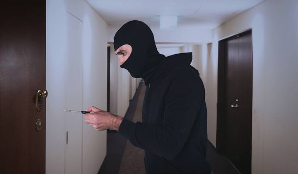 Ladrão com balaclava tenta abrir a porta do apartamento com uma chave - Foto, Imagem