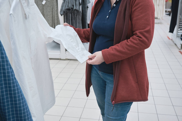 Raskaana oleva nainen myymälässä valitsee uuden valkoisen liike-paita miehelleen - Valokuva, kuva