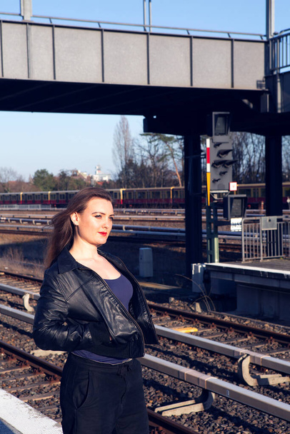 young woman in leather jacket waiting on platform at train station - Фото, изображение