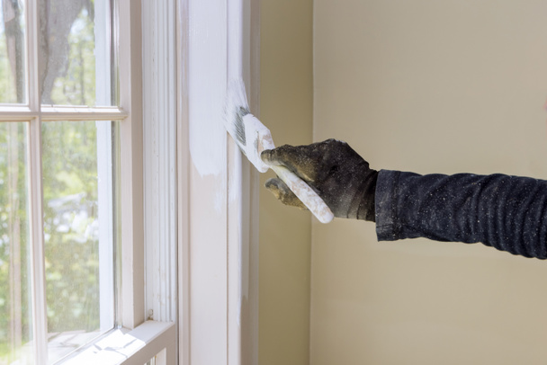 Home renovatie in de klusjesman verft met een laag witte verf borstel een raam molding frame - Foto, afbeelding