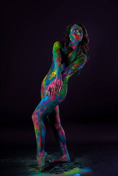 Bright colorful body art on black background, sexy nude woman painted with powder paints, studio shot - Фото, изображение