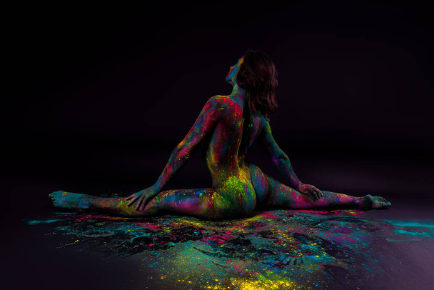 Bright colorful body art on black background, sexy nude woman painted with powder paints, studio shot - Foto, Imagen