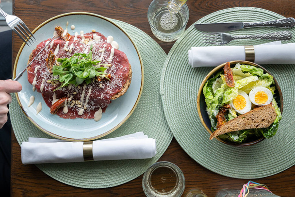 Ужин, вид сверху на обед с салатом и сэндвичем с карпаччо из говядины в роскошном обеденном месте, зеленые плацематы и белые салфетки - Фото, изображение