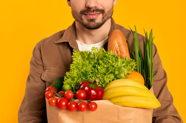 Junger bärtiger Mann mit Gemüsepäckchen auf orangefarbenem Hintergrund. Online Lebensmittel zu Hause bestellen. - Foto, Bild