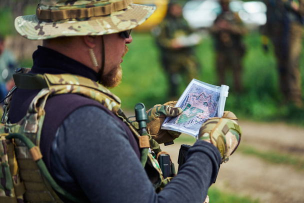 Airsoft speler in militair uniform onderzoekt een kaart - Foto, afbeelding