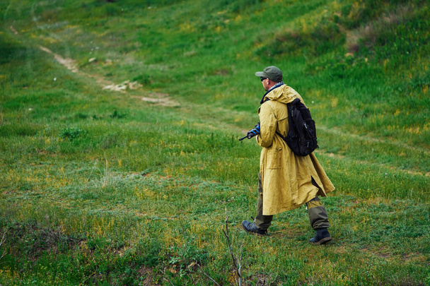 airsoftowiec w żółtym płaszczu przechodzi przez pole z bronią w ręku. - Zdjęcie, obraz