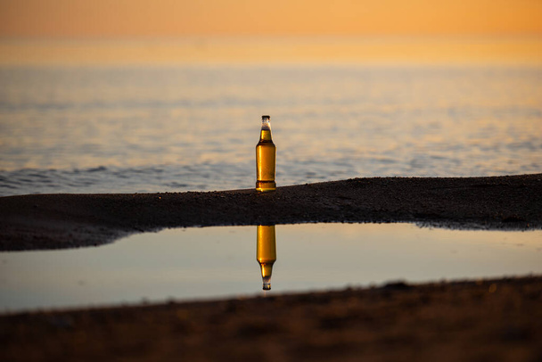 Пляшка пива на пляжі під час заходу сонця
 - Фото, зображення