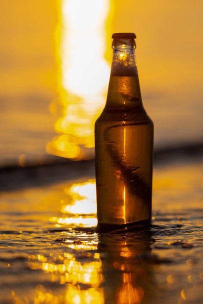 Butelka piwa w oceanie wody morskiej z bokeh w tle - Zdjęcie, obraz
