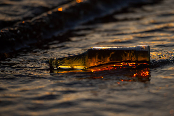 Felborult sörösüveg naplemente tengervíz bokeh a háttérben, és vakító a vízben. - Fotó, kép