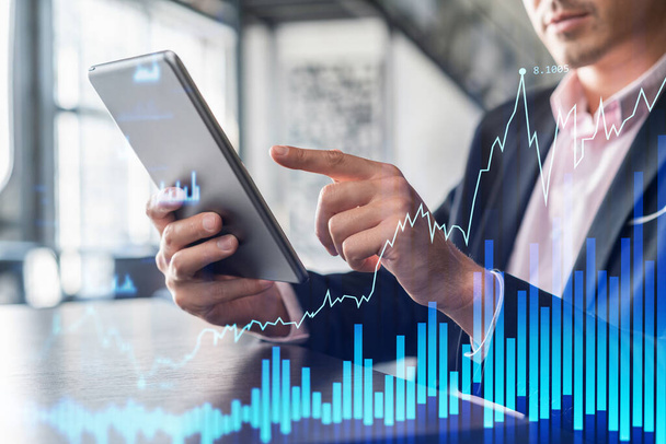 Businessman in suit using tablet device to optimize trading strategy at corporate finance fund. Forex chart hologram over modern panoramic office background - Fotoğraf, Görsel