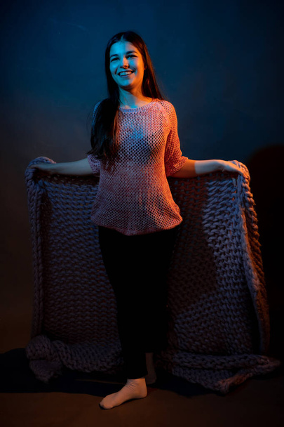 Girl in pink sweater with pink plaid on a dark background with colored light - Foto, imagen
