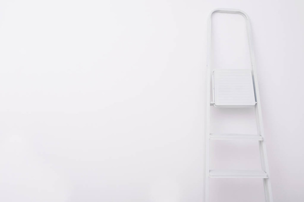 a white folding ladder stands against a clean white wall, on the left is a place for your lettering - Foto, Imagem