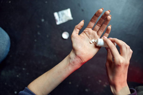 Μια ναρκομανής κρατάει χάπια, σκόνη σε ταχυδρομικό πακέτο στο παρασκήνιο. Ναρκωτικά εθισμός πρόβλημα, αιώνια κατάθλιψη των τοξικομανών ανθρώπους, έννοια πρεζόνι - Φωτογραφία, εικόνα