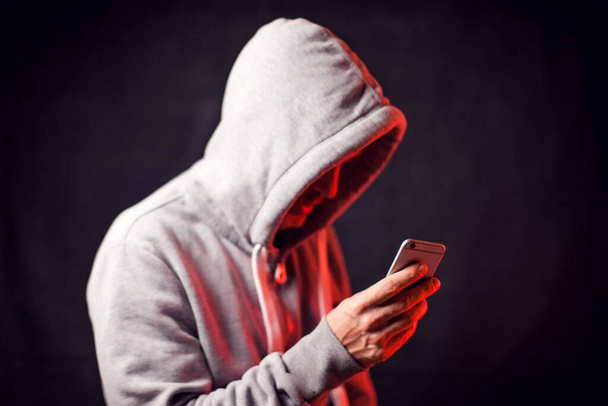 Mężczyzna w bluzie z kapturem z telefonem komórkowym w rękach. Koncepcja przestępczości i hakowania - Zdjęcie, obraz