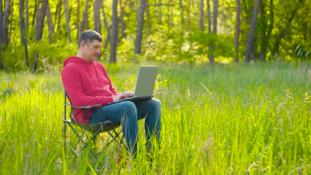 Человек, работающий на ноутбуке в летнем лесу - Кадры, видео